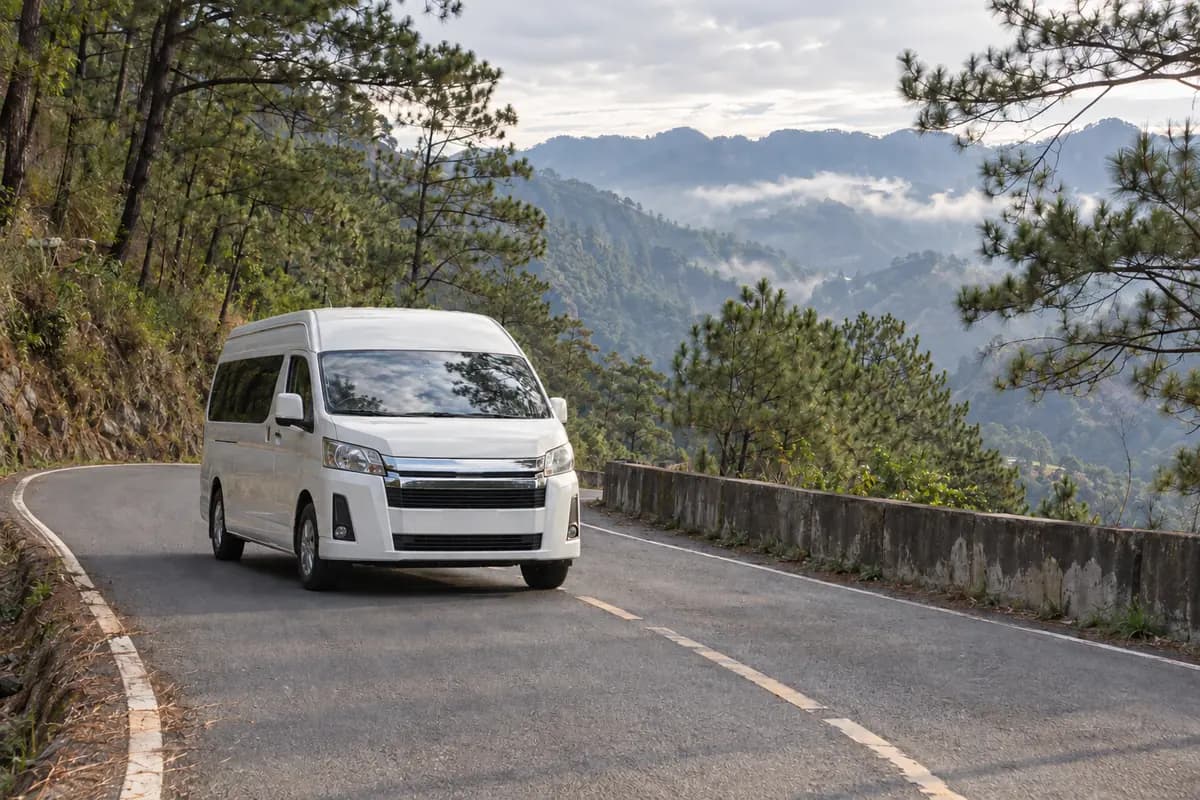 White passenger van on a winding mountain road through misty pine forest
