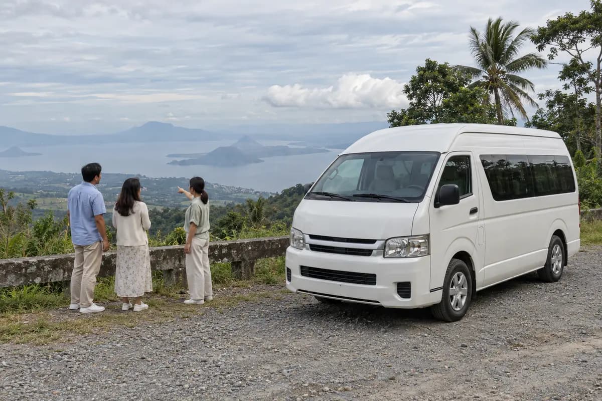 Travellers at a ridge-top lookout beside a white passenger van, with a hazy lake and volcanic island below